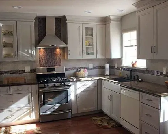 Bright modern kitchen with white cabinets, stainless stove, gray counters, and a tiled backsplash  In Bucks County PA