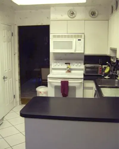 Small white kitchen with a microwave over the stove, black countertop, and an open doorway to a dark room. In Bucks County PA