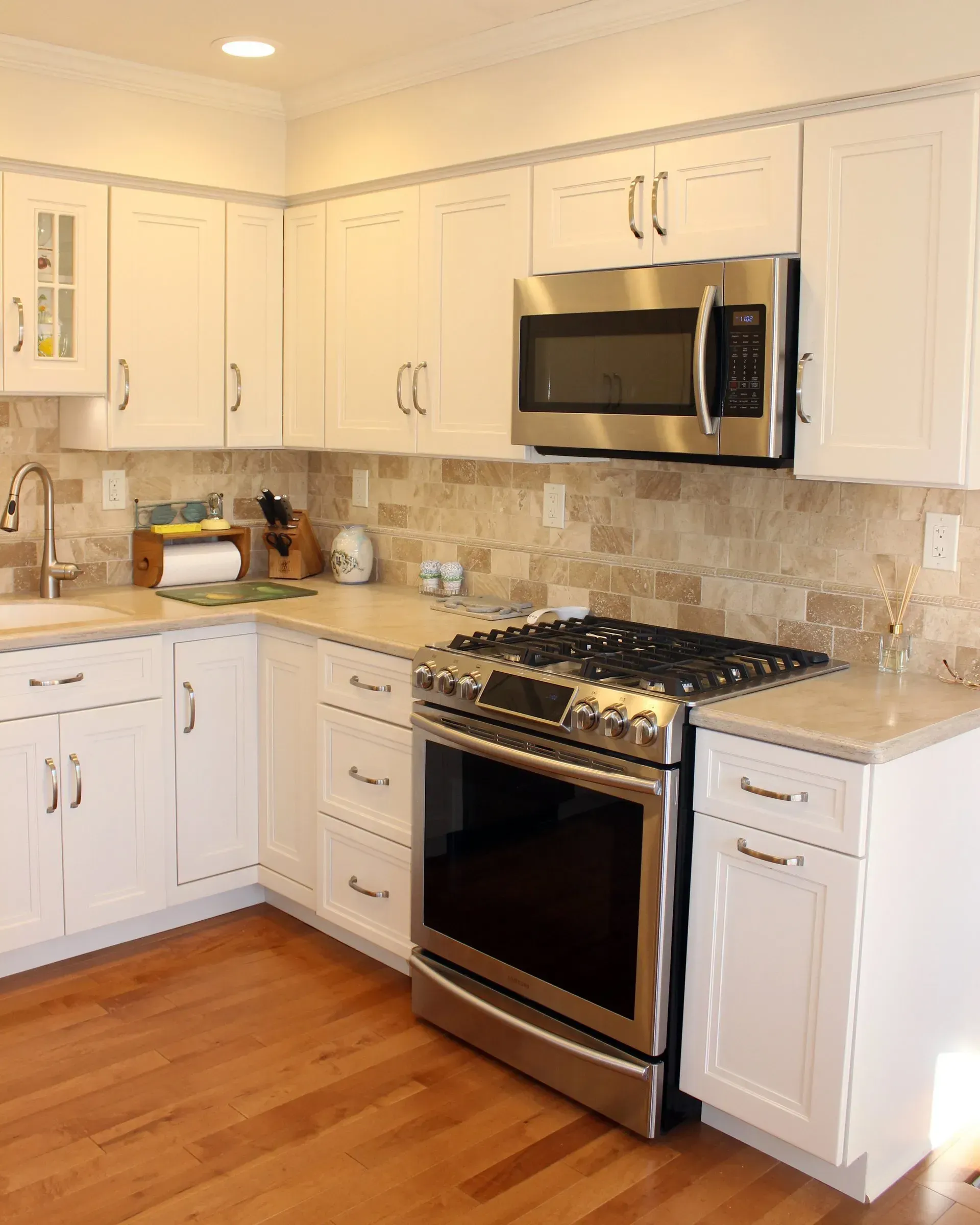 Bright white kitchen with stainless steel stove and microwave, white cabinets, stone backsplash, and hardwood floor  In Bucks County PA