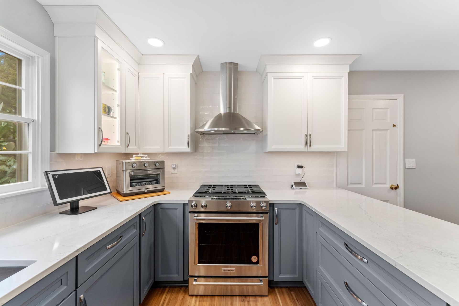 Bright white kitchen with blue lower cabinets, stainless stove, range hood, and wood floor In Bucks County PA