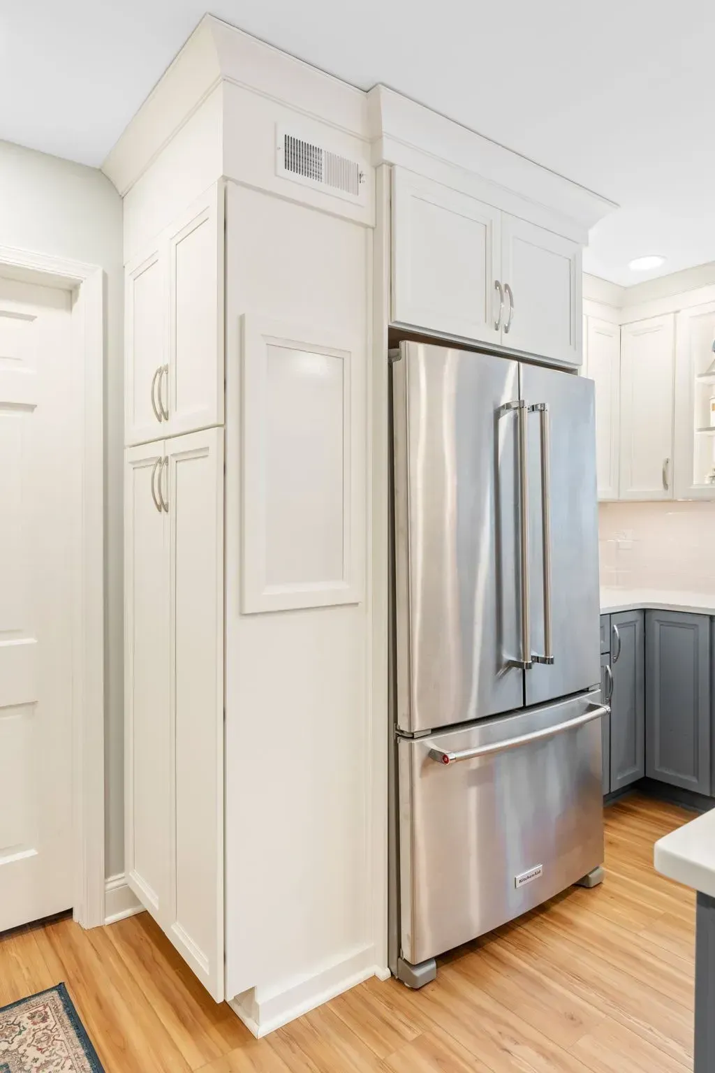 Bright kitchen with a stainless steel refrigerator, white cabinets, and wood flooring In Bucks Country PA