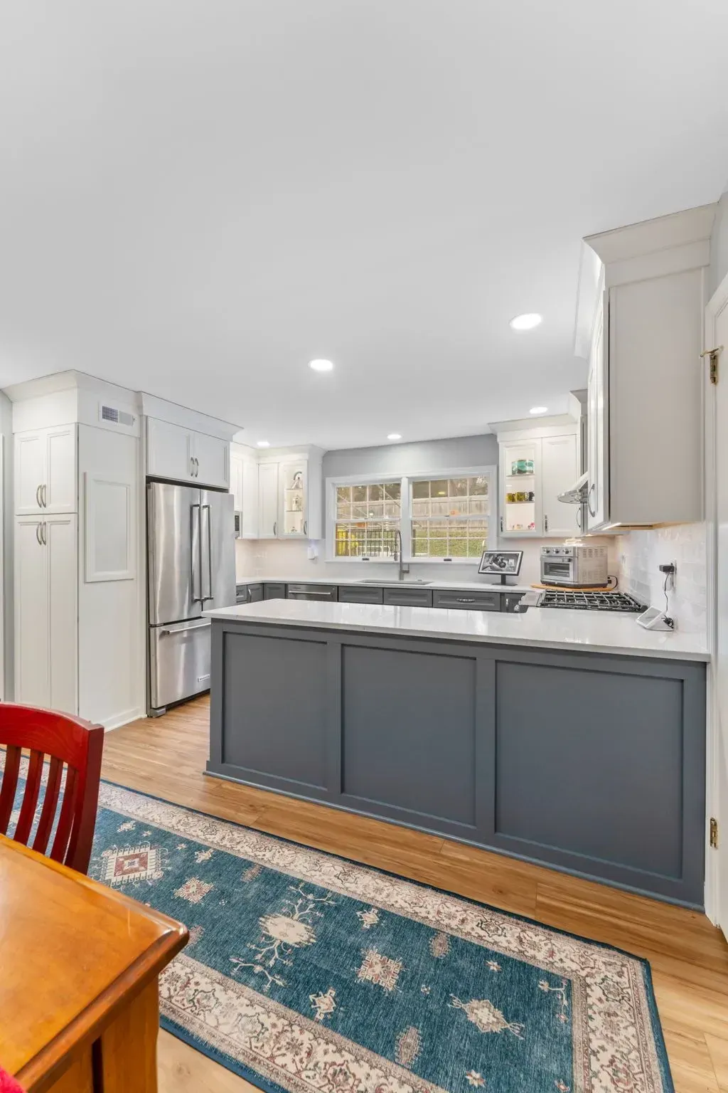 Bright modern kitchen with gray island, stainless fridge, white cabinets, and blue patterned rug In Bucks Country PA