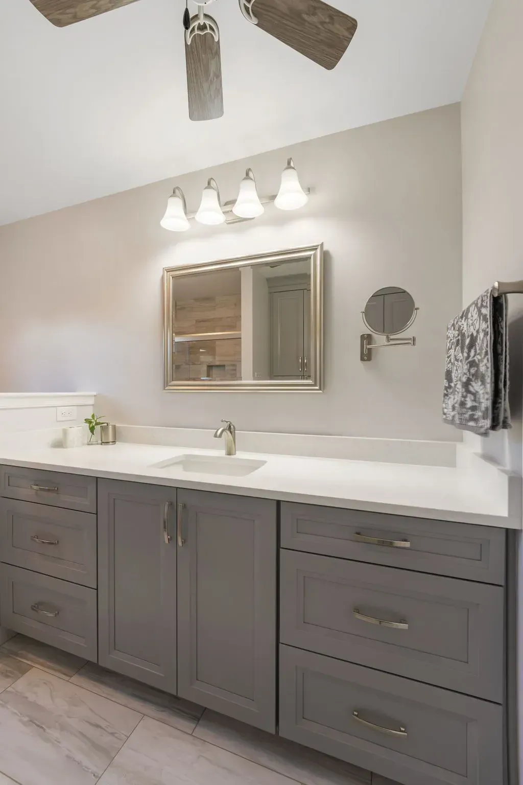 Gray bathroom vanity with white countertop, double sinks, wall mirror, lights, and ceiling fan In Bucks County PA