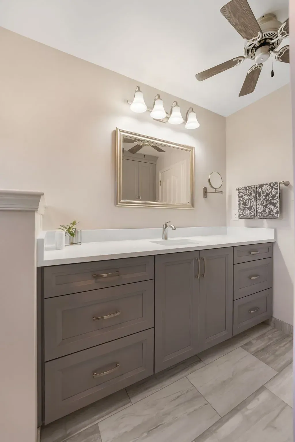 Gray bathroom vanity with white countertop, mirror, lights, and ceiling fan on gray tile floor In Bucks County PA