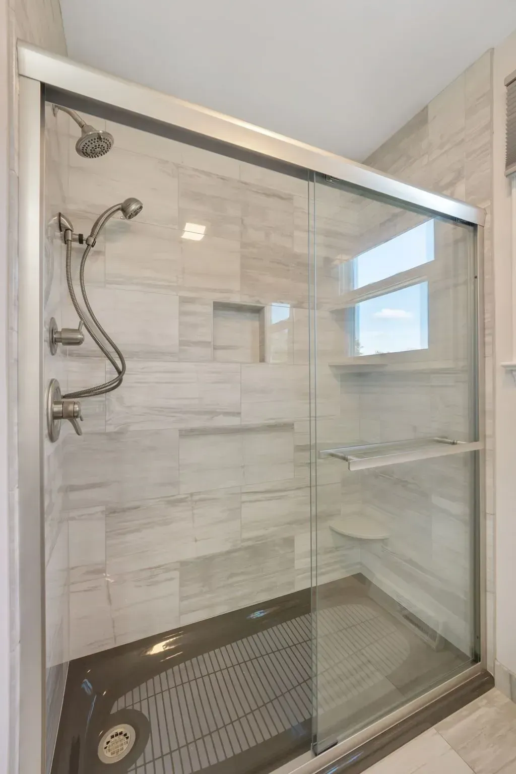 Modern glass-enclosed shower with beige tile walls and a built-in shelf In Bucks County PA