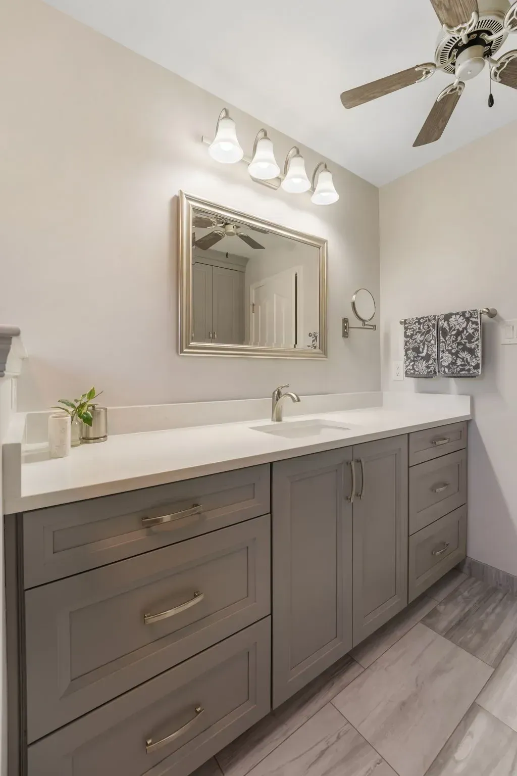 Modern gray bathroom vanity with double sink, mirror, lights, and ceiling fan in a bright room In Bucks County PA