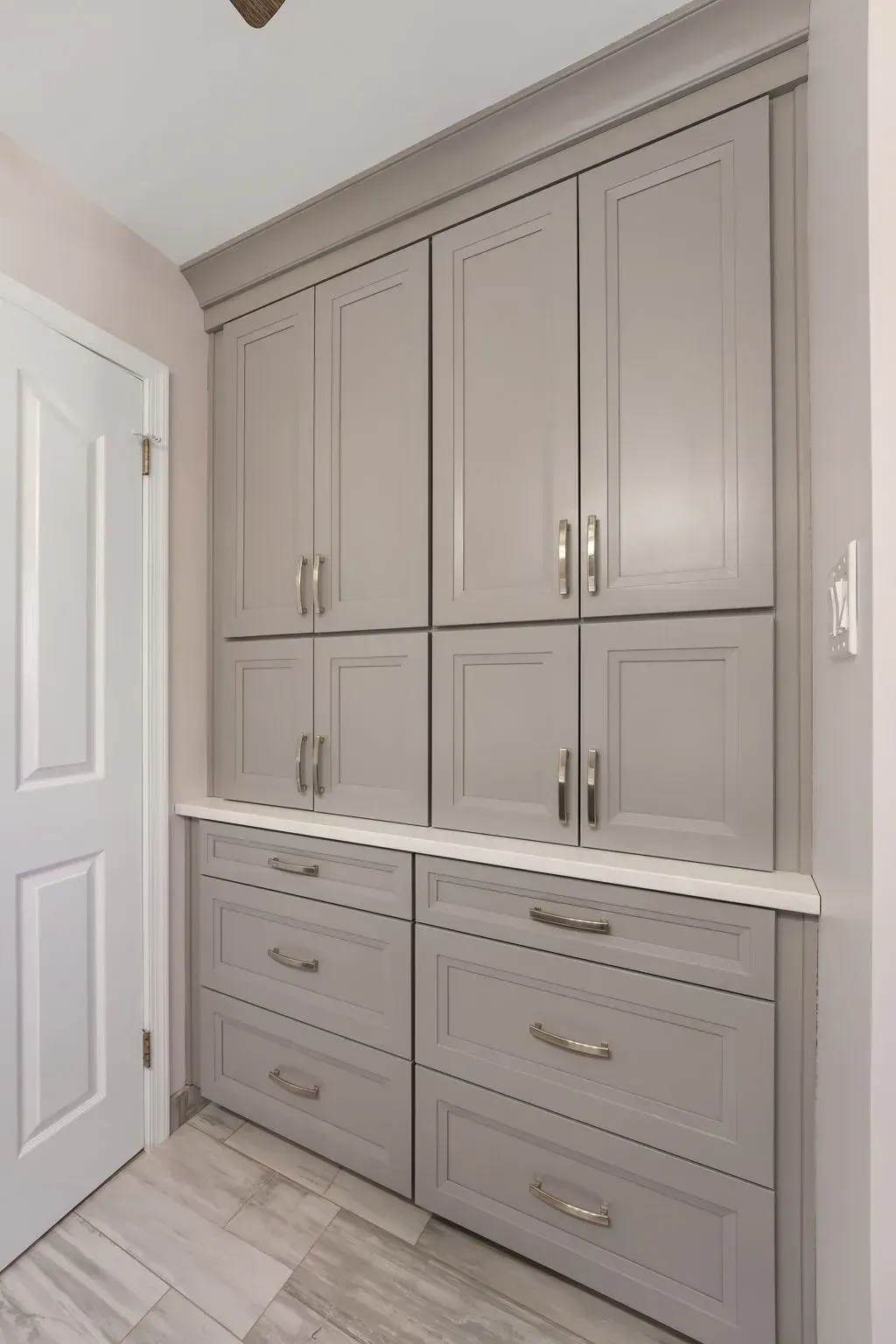 Built-in beige cabinets and drawers in a narrow hallway or closet area with a white door and light wood floor In Bucks County PA