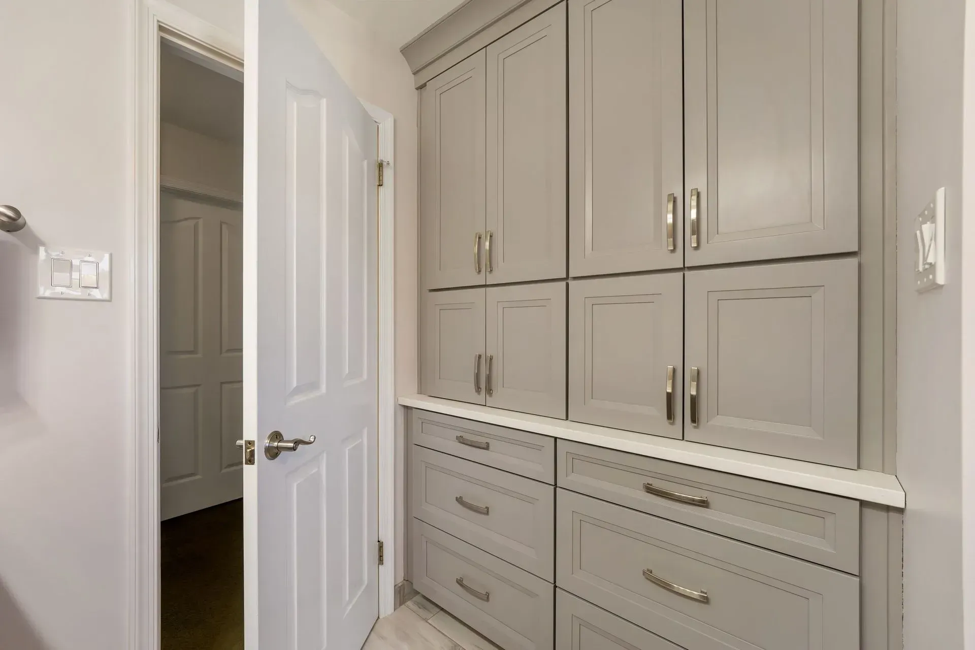 Built-in gray cabinets and drawers in a bright hallway beside an open white door In Bucks County PA