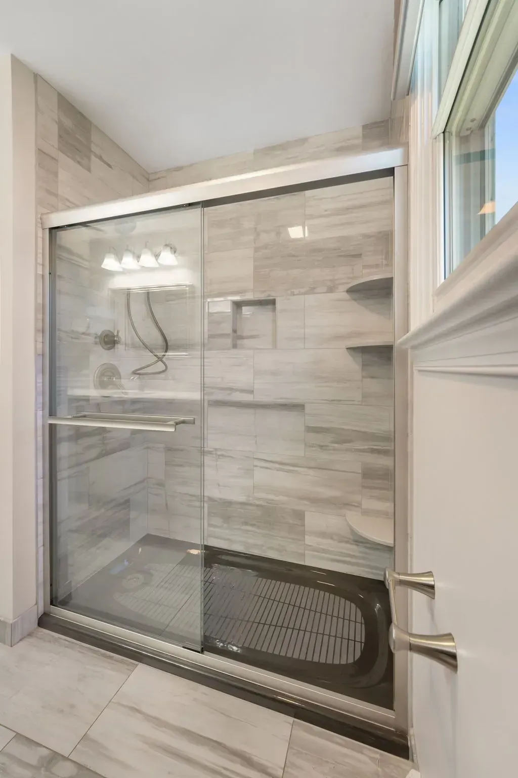 Walk-in shower with sliding glass door, beige tile walls, and built-in shelves in a bathroom In Bucks County PA