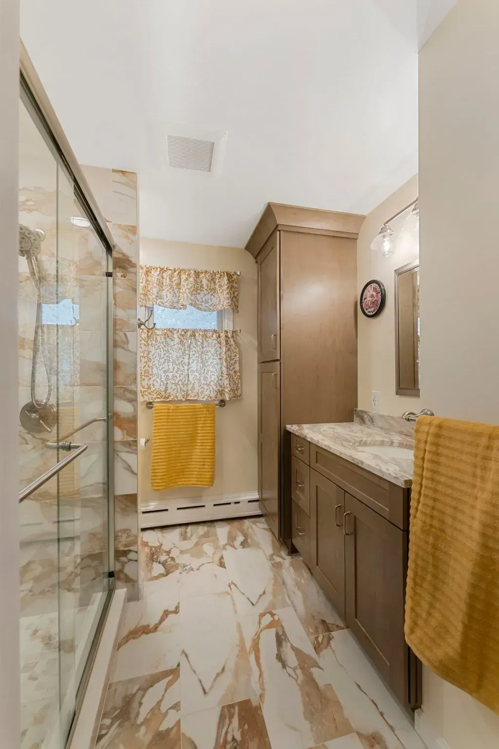 Bright bathroom with glass shower, beige vanity, marble-look floor, and yellow towels In Bucks County PA