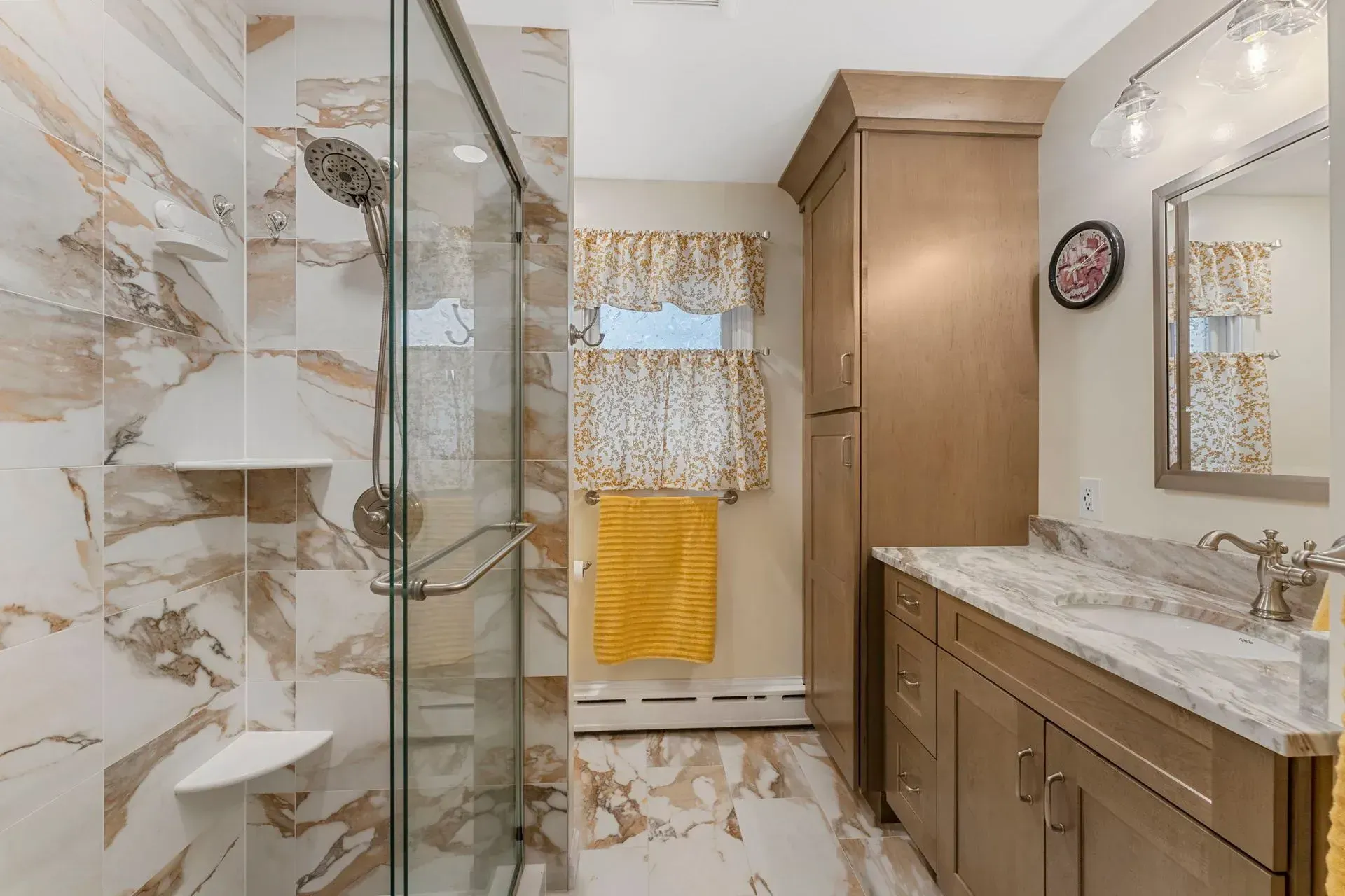 Modern bathroom with marble shower, glass enclosure, vanity, and yellow towel by window In Bucks County PA