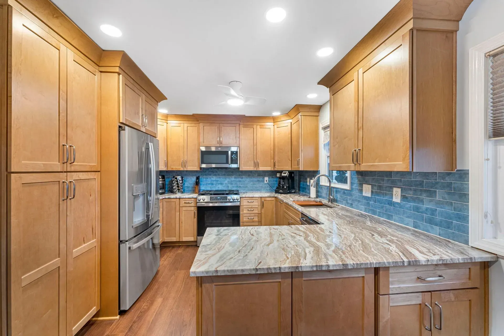 Modern kitchen with wood cabinets, blue tile backsplash, granite island, and stainless steel appliances In Bucks Country PA