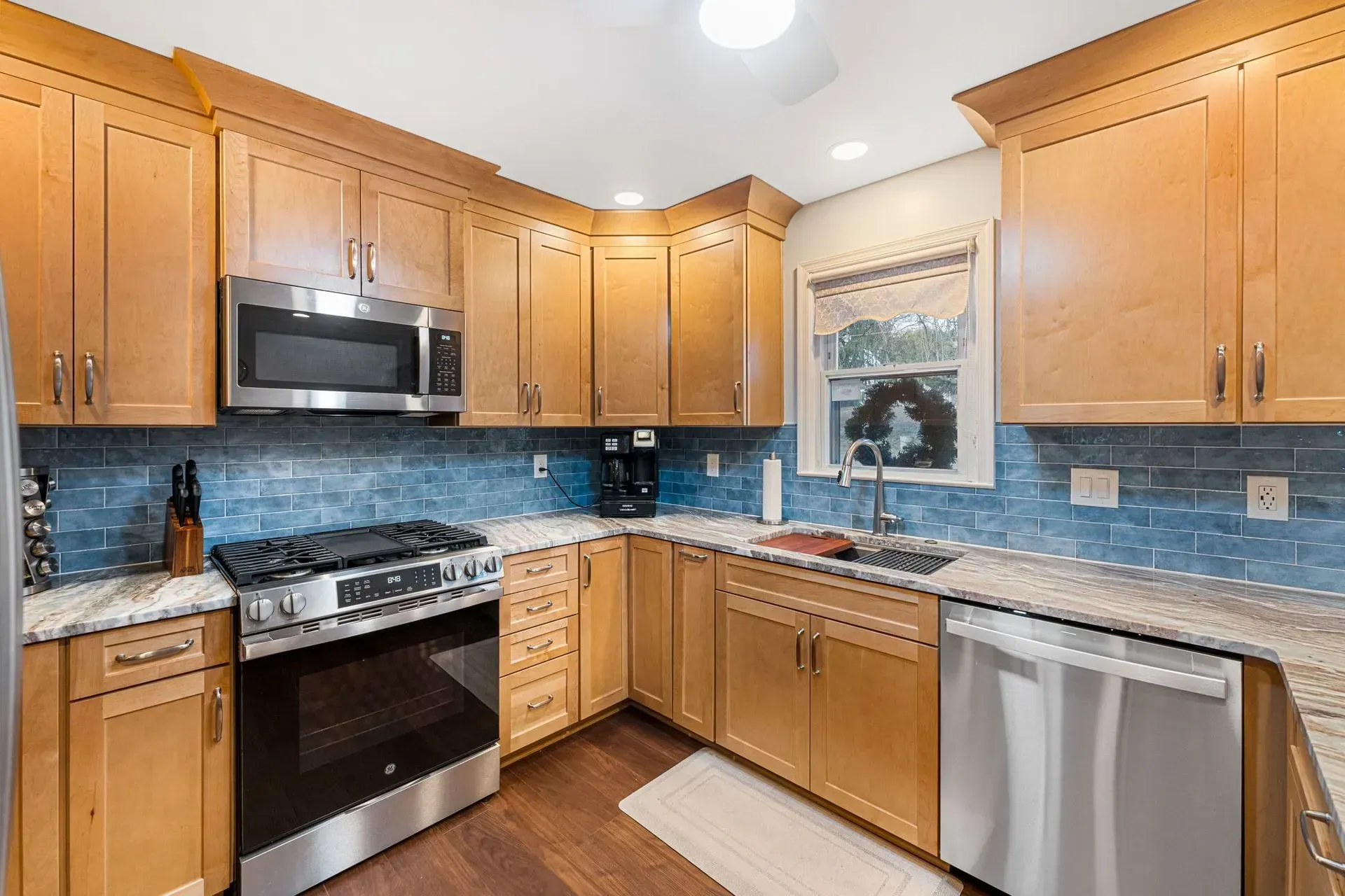 Modern kitchen with wood cabinets, stainless steel appliances, blue tile backsplash, and a window over the sink In Bucks Country PA