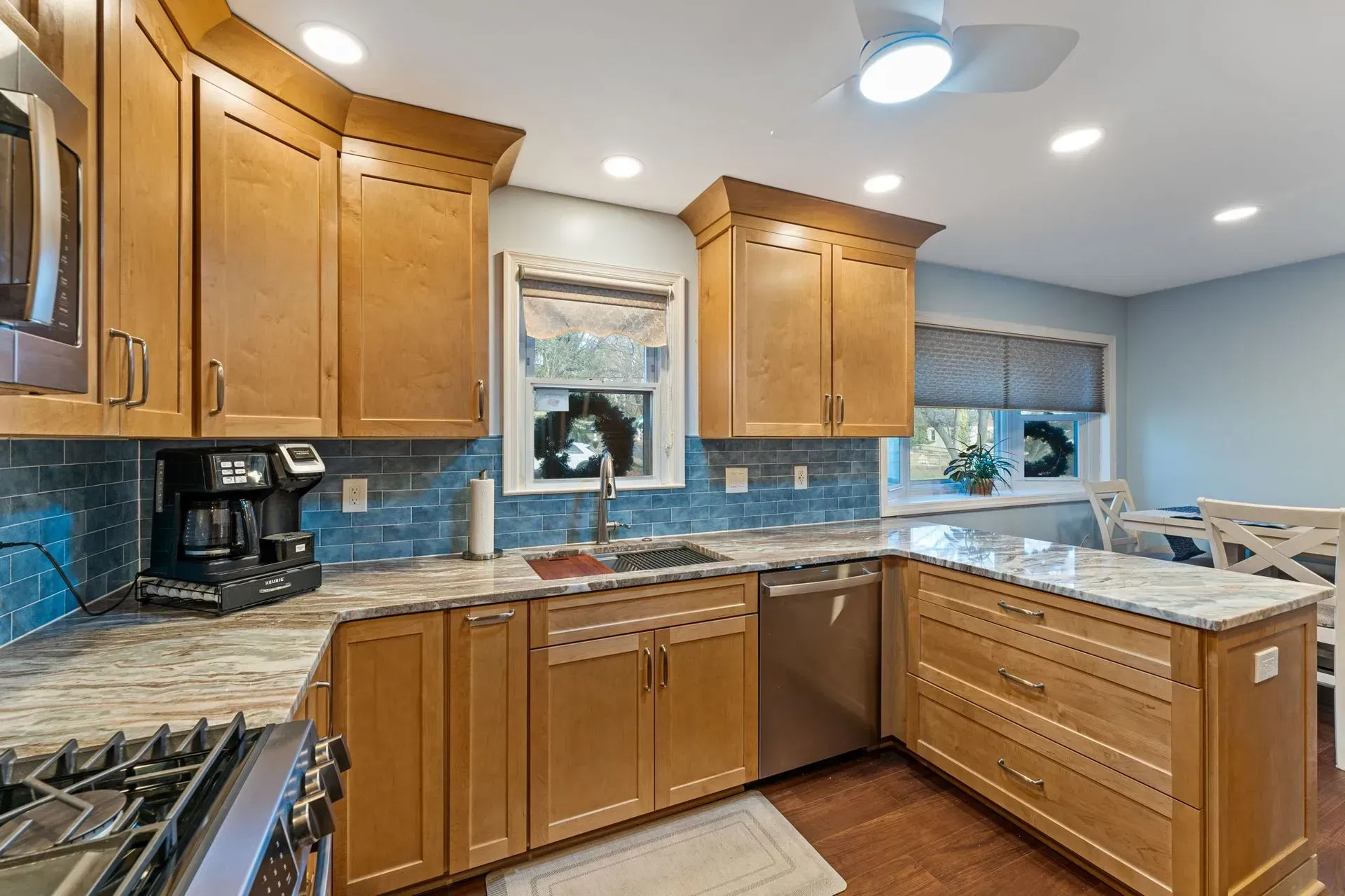 Bright kitchen with wooden cabinets, granite counters, blue tile backsplash, and stainless stove and sink In Bucks Country PA