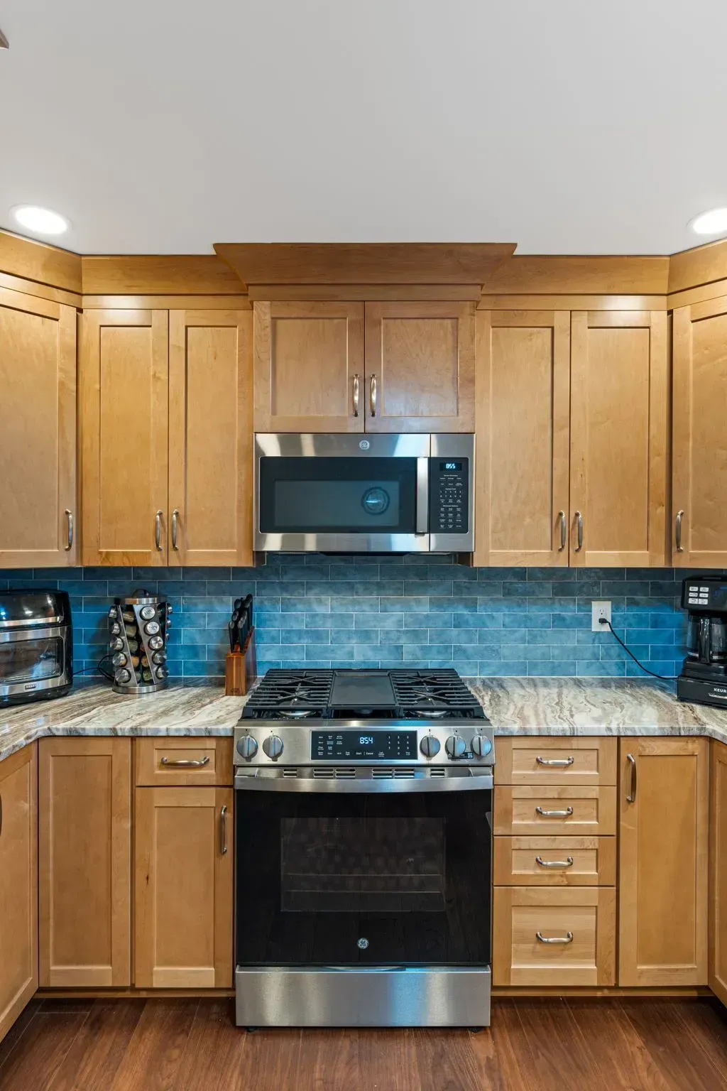 Modern kitchen with wooden cabinets, blue tile backsplash, granite counters, and stainless steel stove and microwave In Bucks Country PA