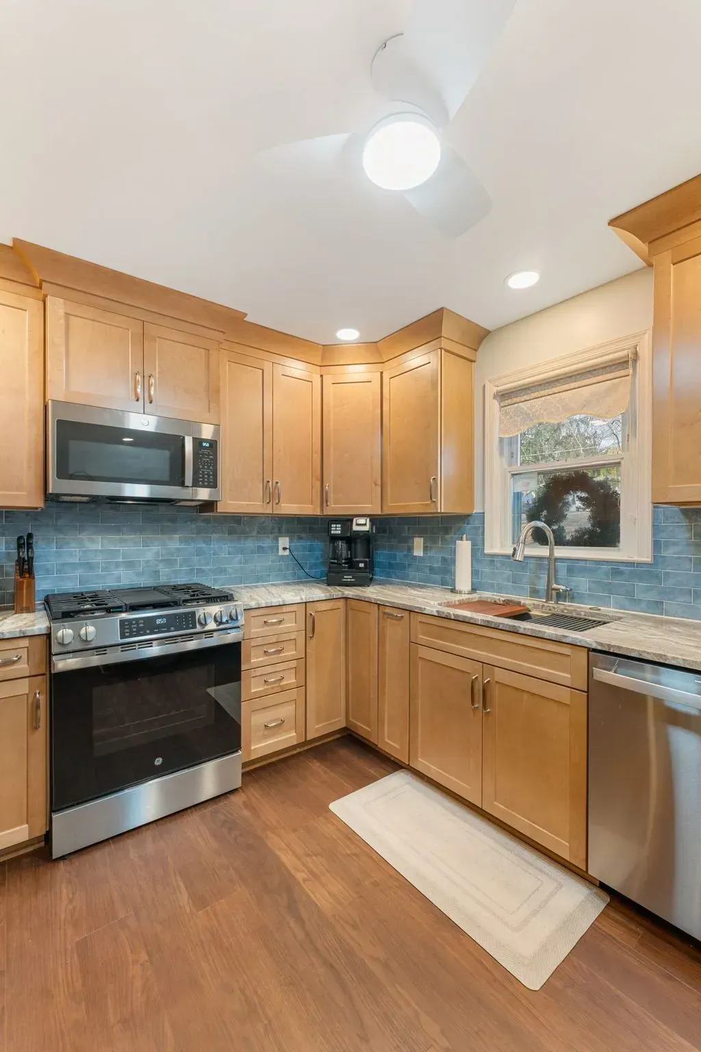Bright kitchen with wood cabinets, stainless appliances, blue tile backsplash, and a window over the sink In Bucks Country PA