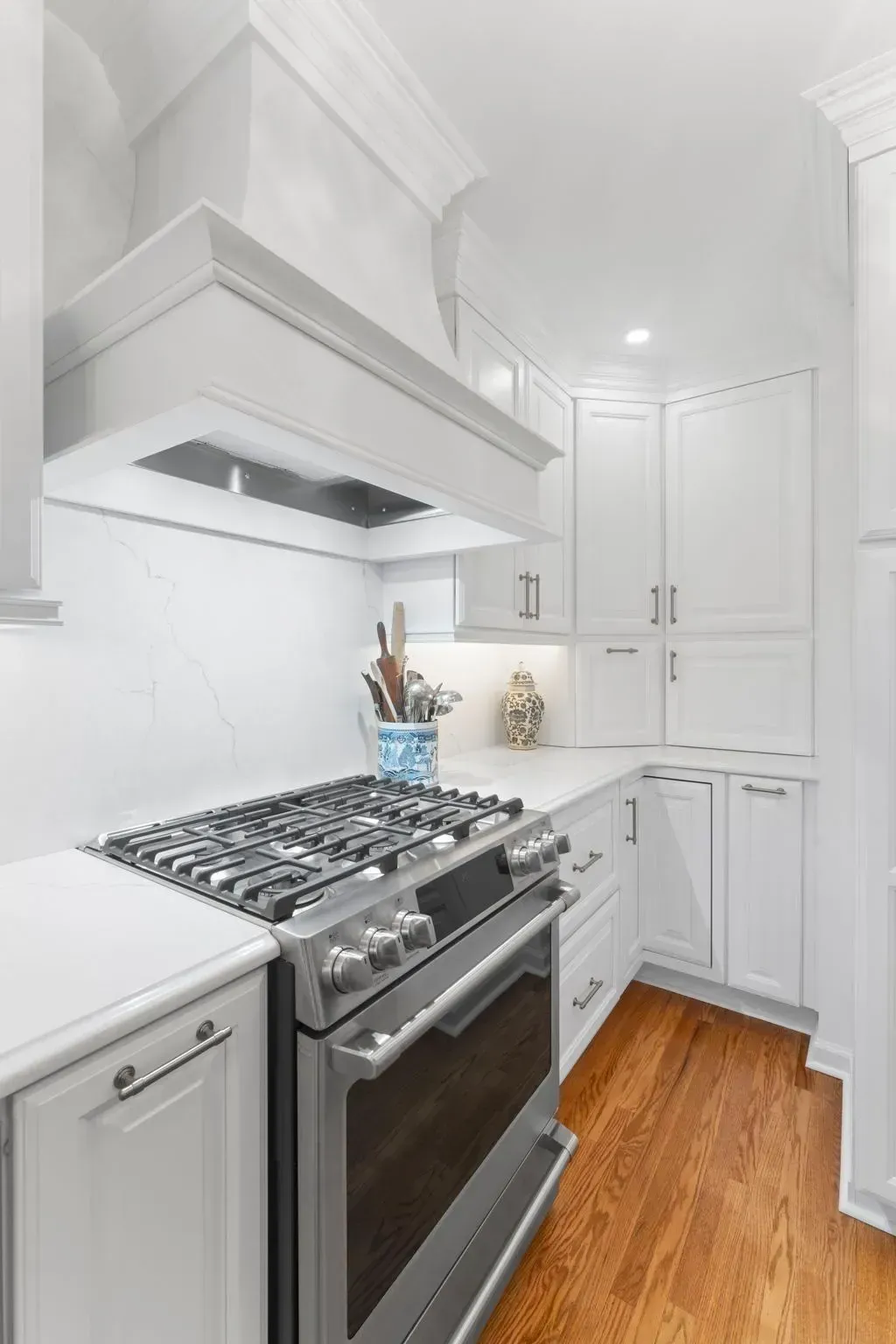 Bright white kitchen with stainless steel stove, white cabinets, and warm wood floor  In Bucks County PA