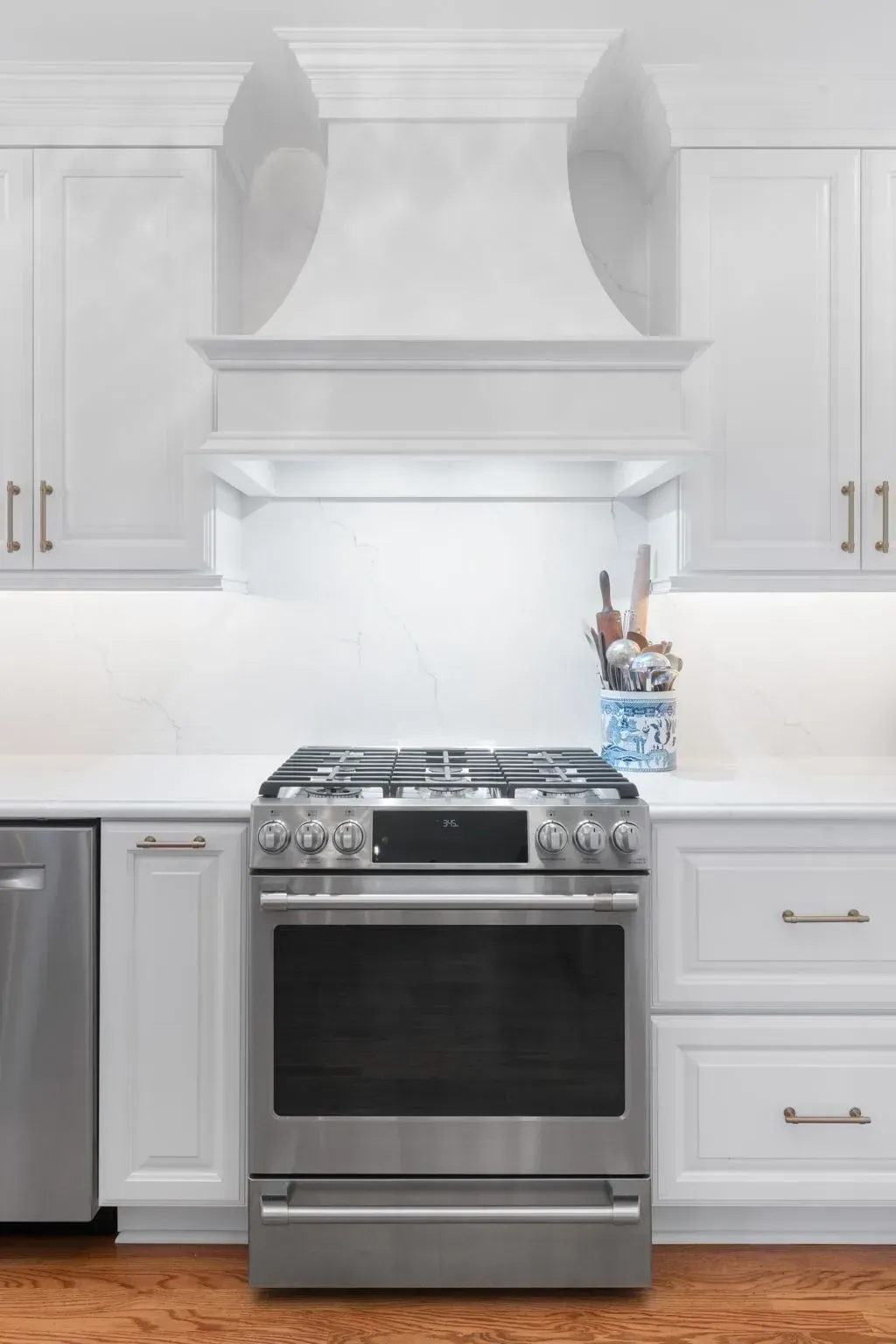 White kitchen with stainless steel range and hood, gray cabinets, and utensil holder on the counter  In Bucks County PA