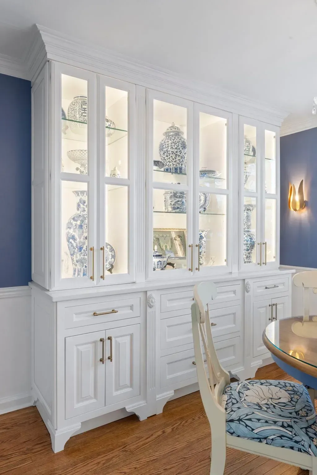 White built-in cabinets with glass doors in a blue dining room, with a table and chair in the foreground  In Bucks County PA
