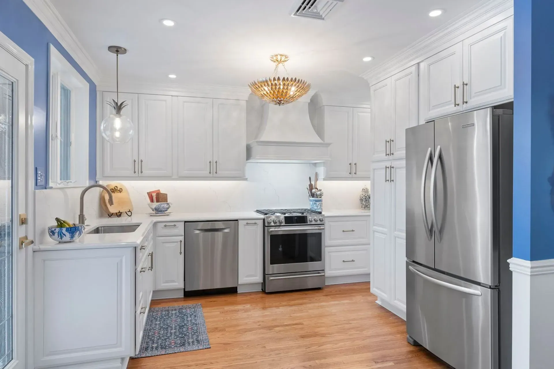 Bright white kitchen with stainless steel appliances, wood floor, blue walls, and a chandelier  In Bucks County PA