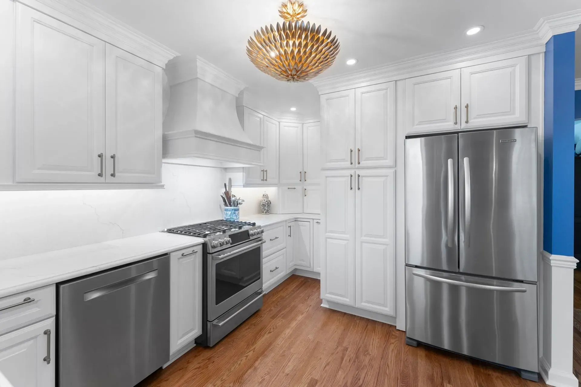 Bright white modern kitchen with stainless steel appliances, wood floor, and gold chandelier  In Bucks County PA
