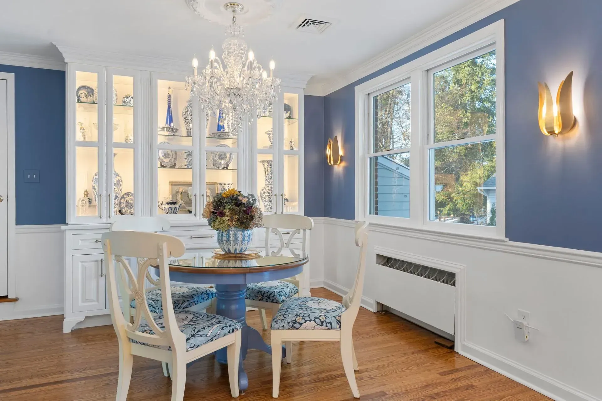 Bright dining room with blue walls, white trim, chandelier, round table, and large windows  In Bucks County PA