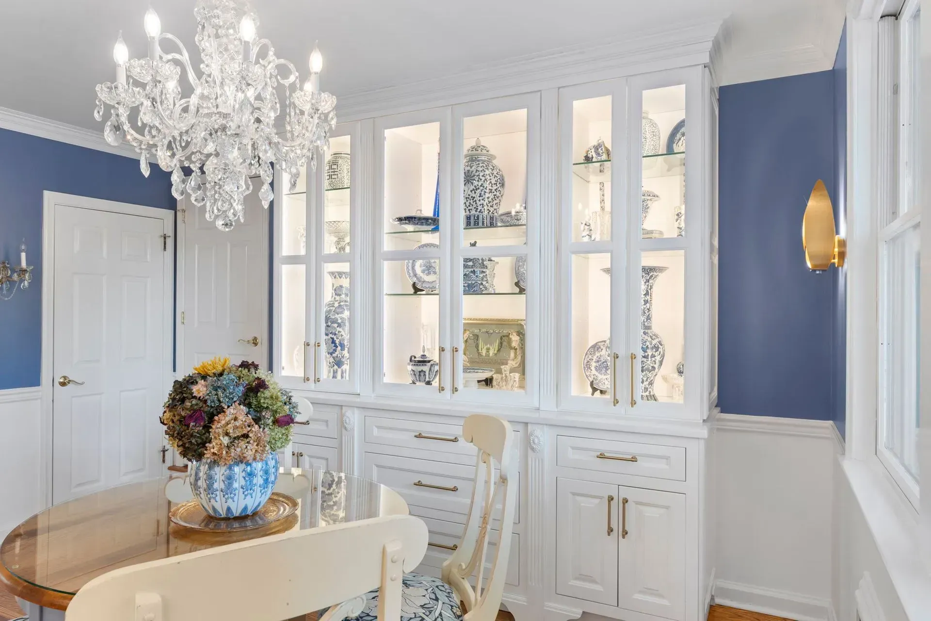 Elegant dining room with white china cabinets, blue walls, chandelier, and round table with floral centerpiece  In Bucks County PA