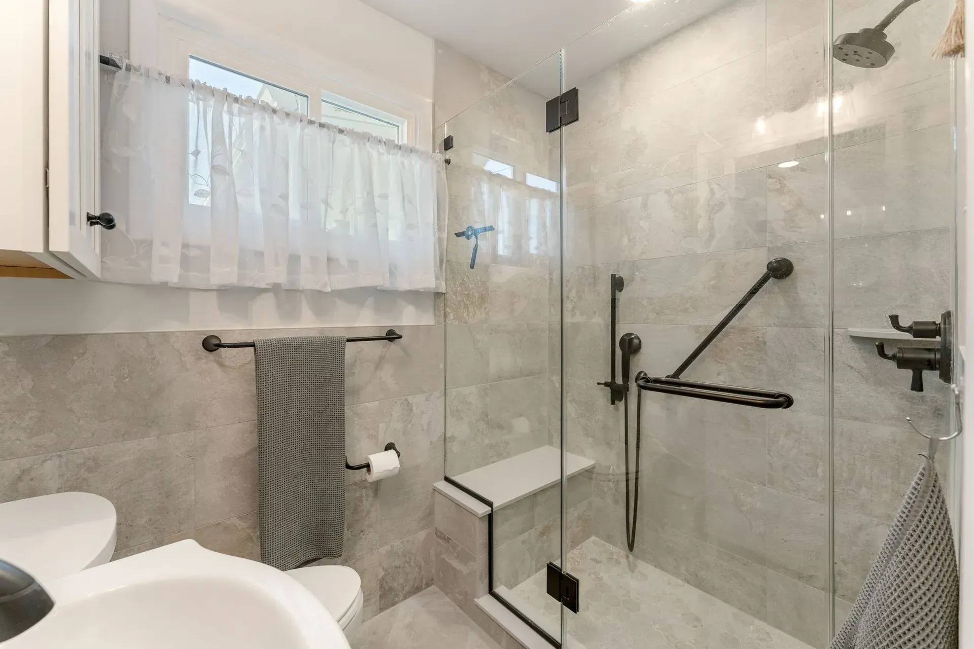 Modern bathroom with glass shower, beige tile, window, and towel rack  In Bucks County PA