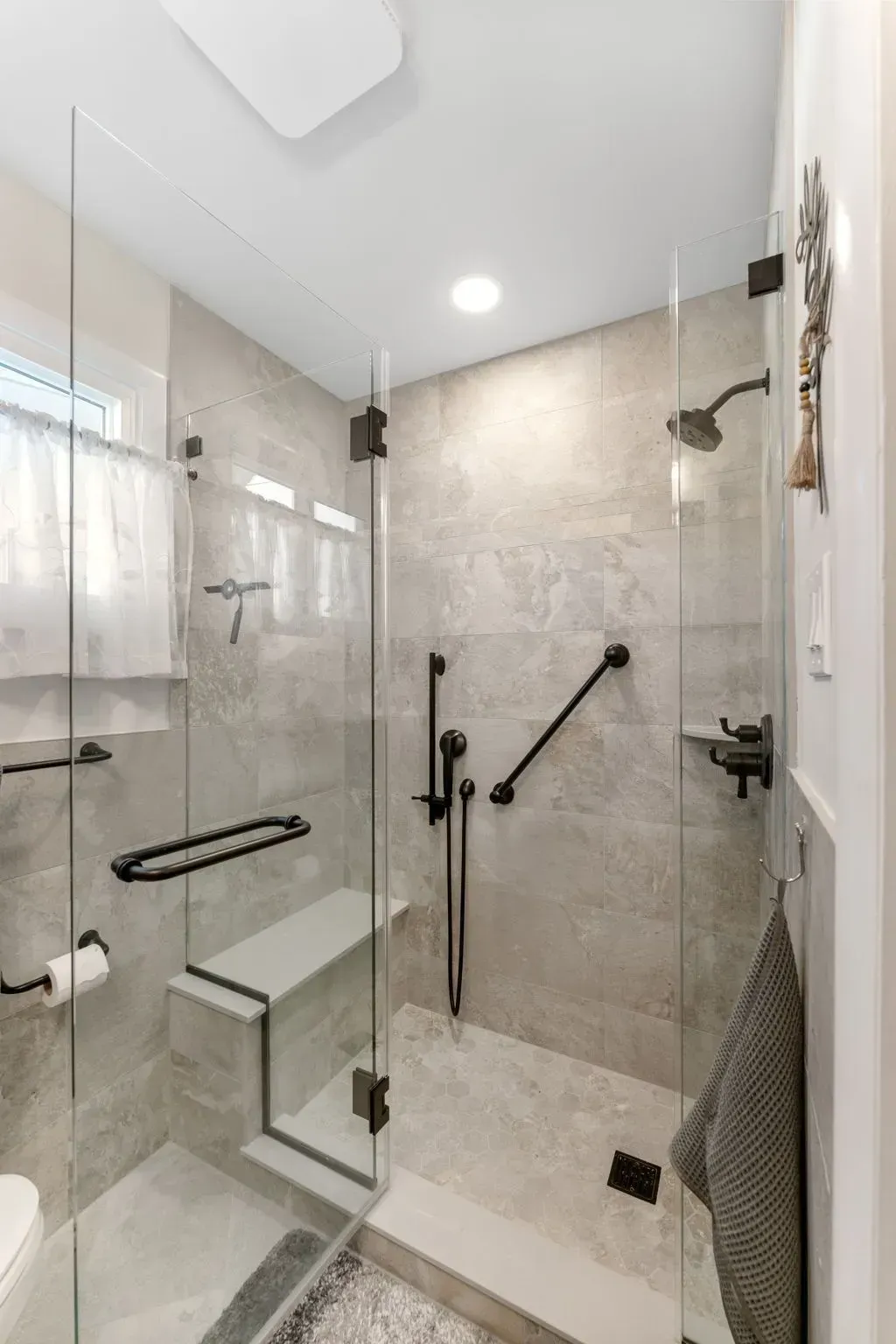 Modern tiled walk-in shower with glass enclosure, grab bars, built-in bench, and handheld showerhead  In Bucks County PA
