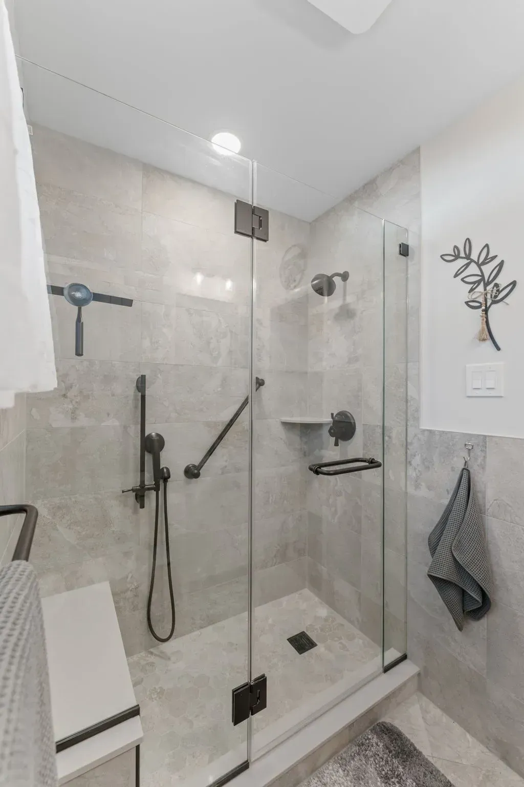 Modern beige tile bathroom with glass shower enclosure, handheld shower, and wall decor  In Bucks County PA