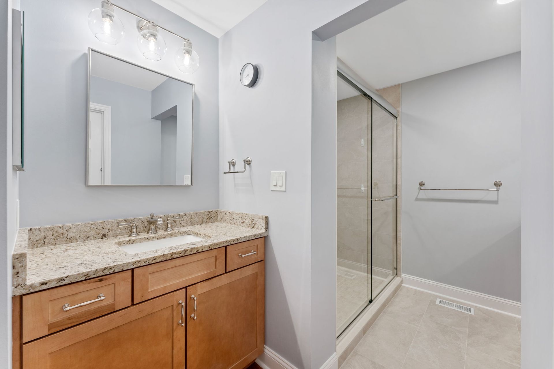 Bathroom with granite vanity, mirror, and glass-enclosed shower in light gray tones In Bucks County PA