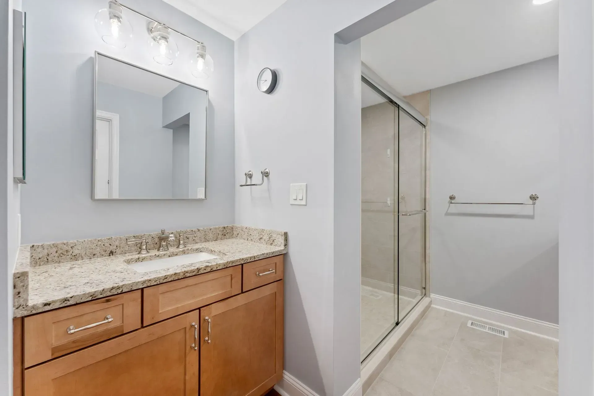 Bathroom with granite vanity, mirror, and glass-enclosed shower in light gray tones  In Bucks County PA