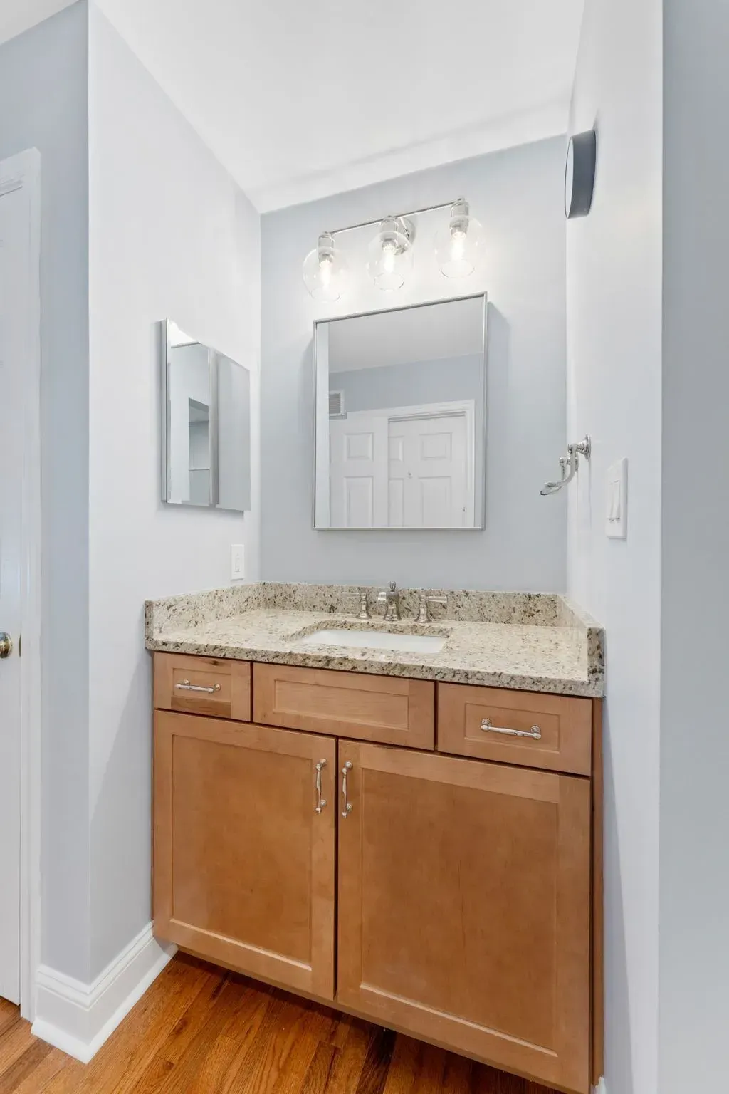 Small bathroom vanity with granite countertop, mirror, light fixture, and white walls in Bucks County PA