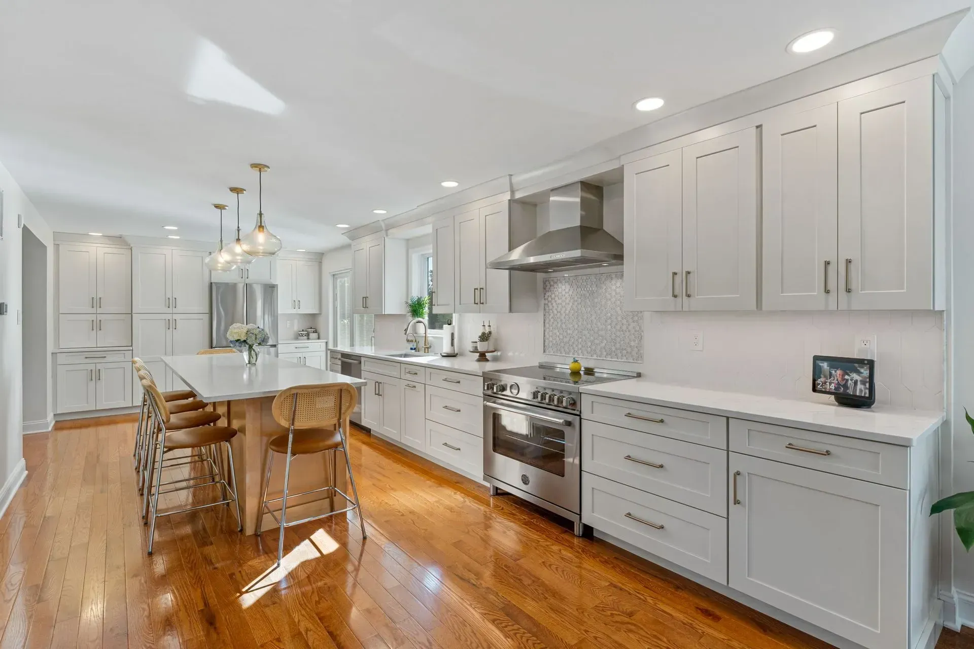 Bright white kitchen with island, stainless appliances, wood floors, and pendant lights In Bucks County PA