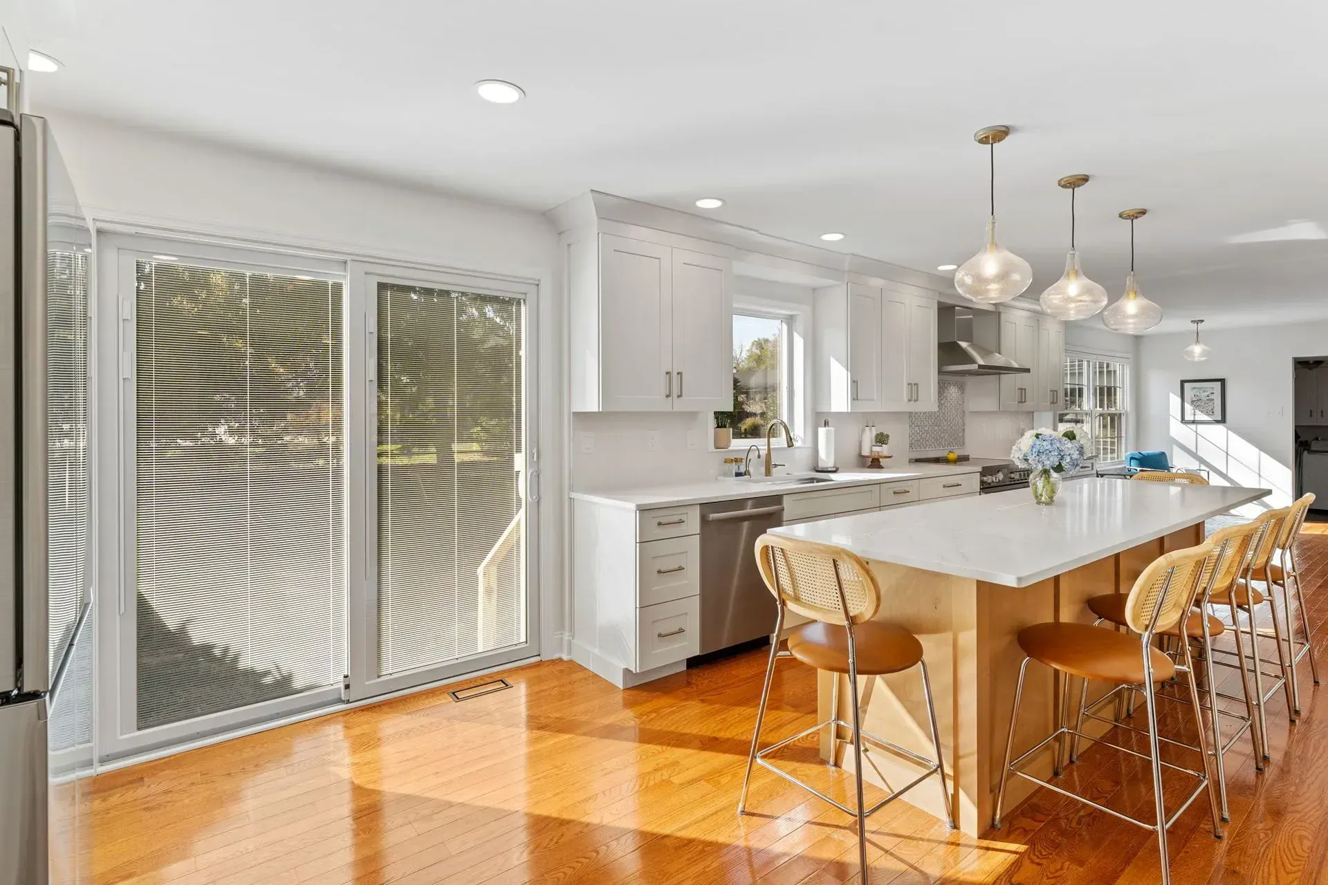 Bright modern kitchen with island, pendant lights, wood floors, and sliding glass doors In Bucks County PA
