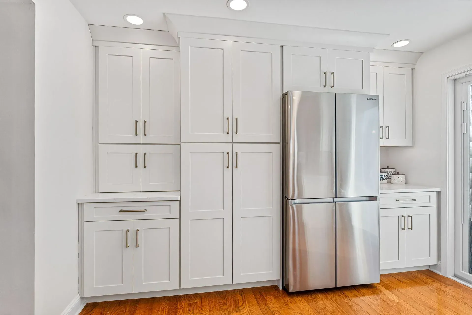 Bright white kitchen with built-in cabinets, stainless steel refrigerator, and hardwood floor In Bucks County PA