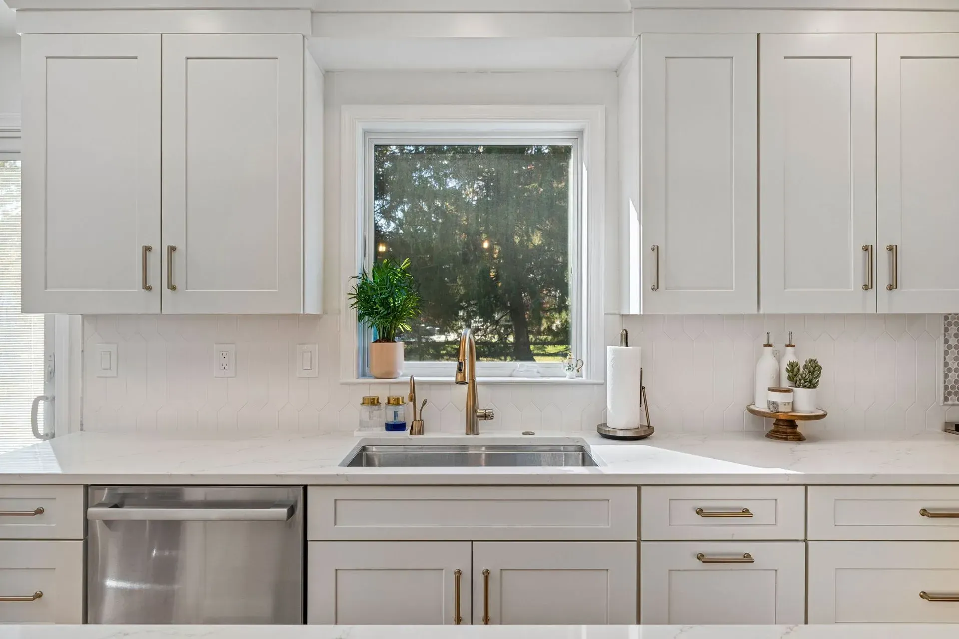Bright white kitchen with window above sink, stainless dishwasher, and cabinets with gold handles In Bucks County PA