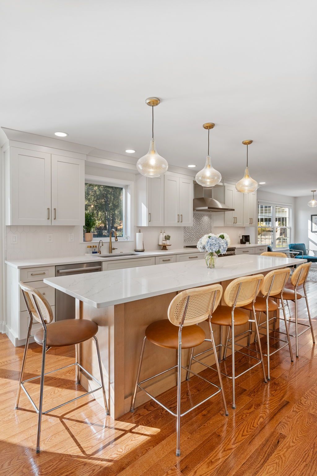 Bright modern kitchen with white island, pendant lights, and four woven bar stools on hardwood floor In Bucks County PA