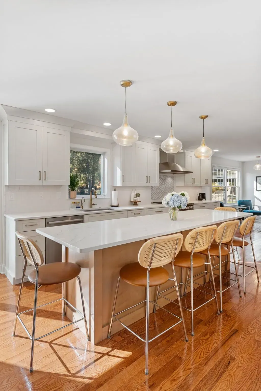 Bright modern kitchen with white island, woven bar stools, gold pendant lights, and hardwood floors In Bucks County PA
