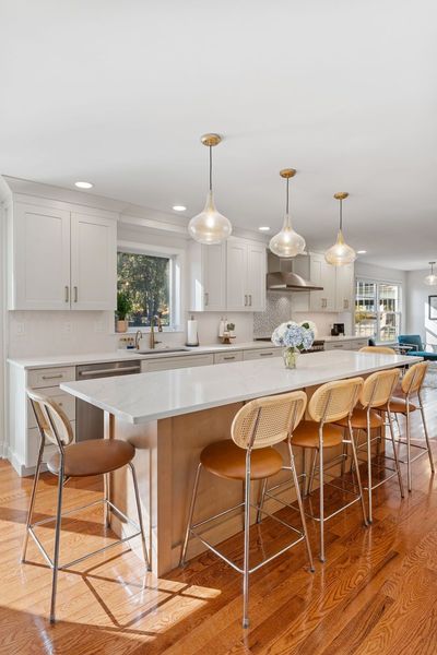 Bright modern kitchen with a white island, pendant lights, bar stools, and wood floors In Bucks County PA