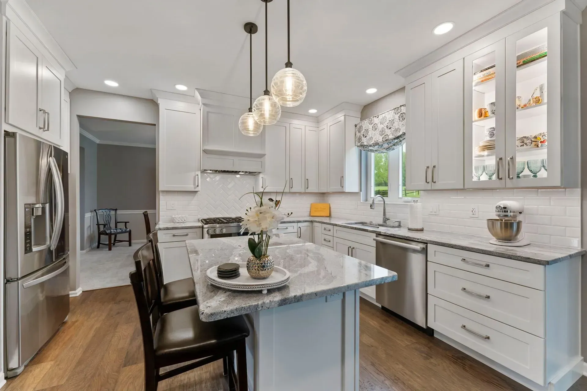 Bright modern white kitchen with island, pendant lights, stainless fridge, and wood floors In Bucks Country PA