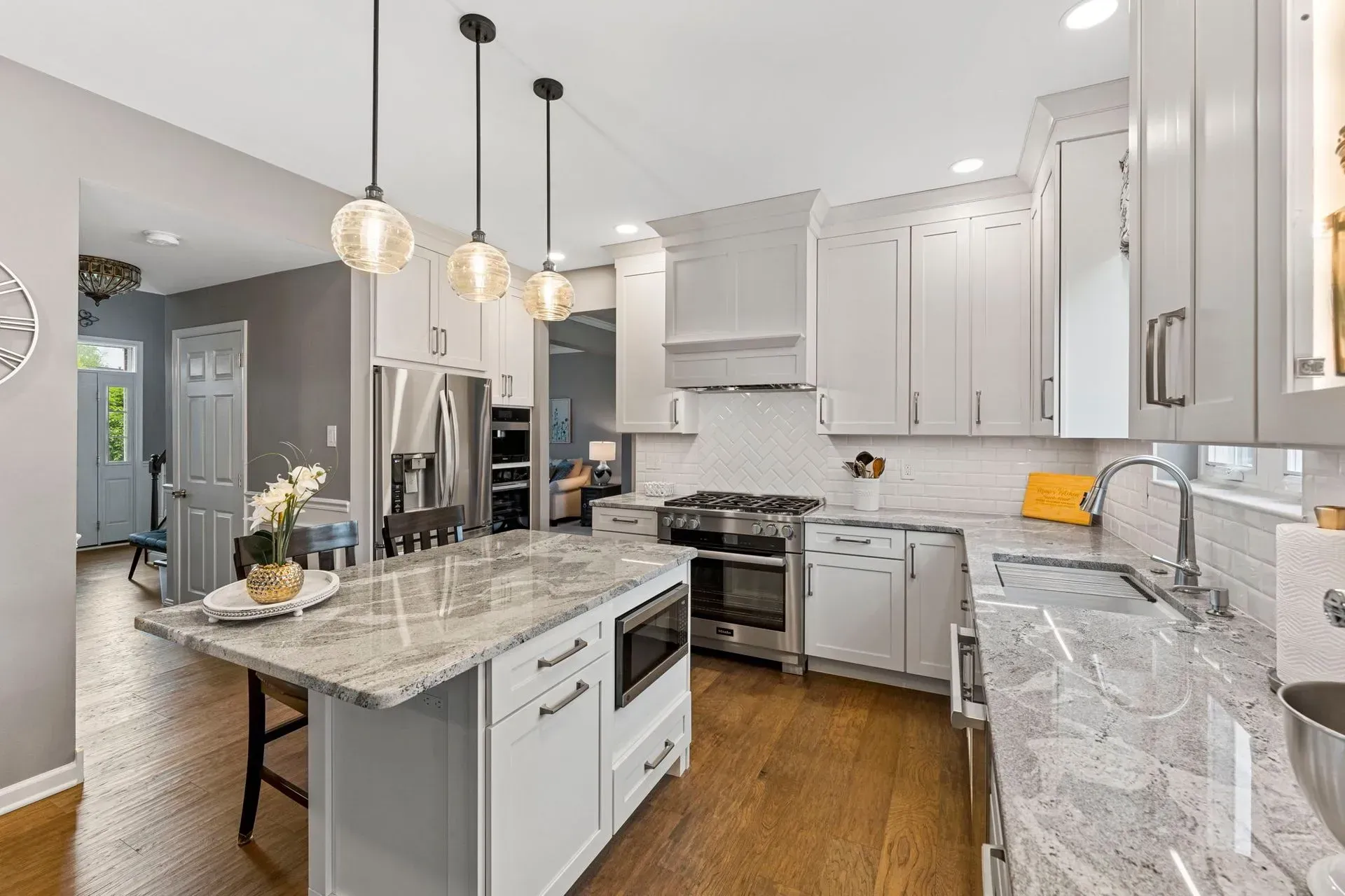 Bright modern kitchen with white cabinets, granite island, stainless steel appliances, and pendant lights