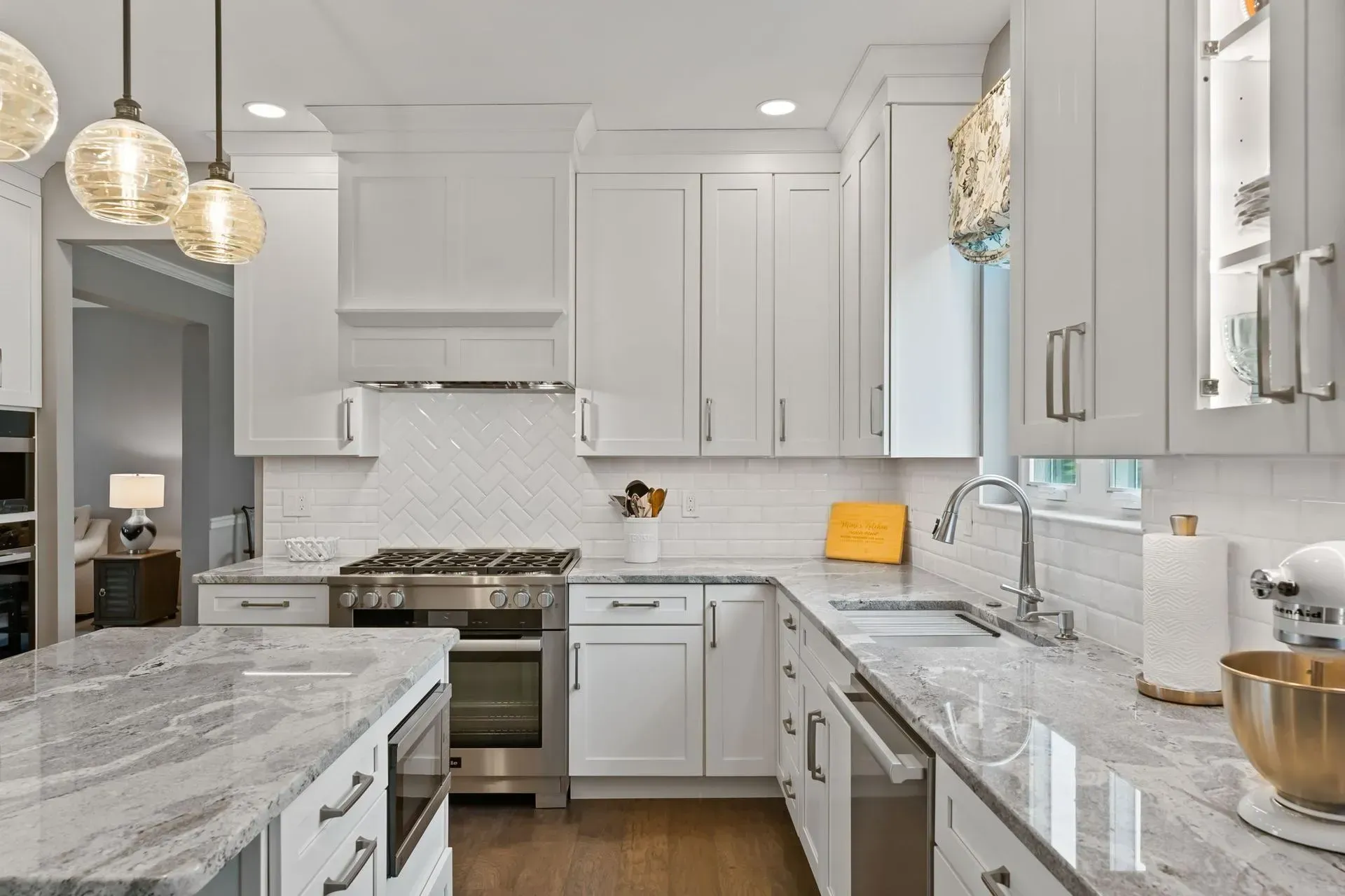 Bright white kitchen with marble countertops, stainless stove, and pendant lights In Bucks Country PA
