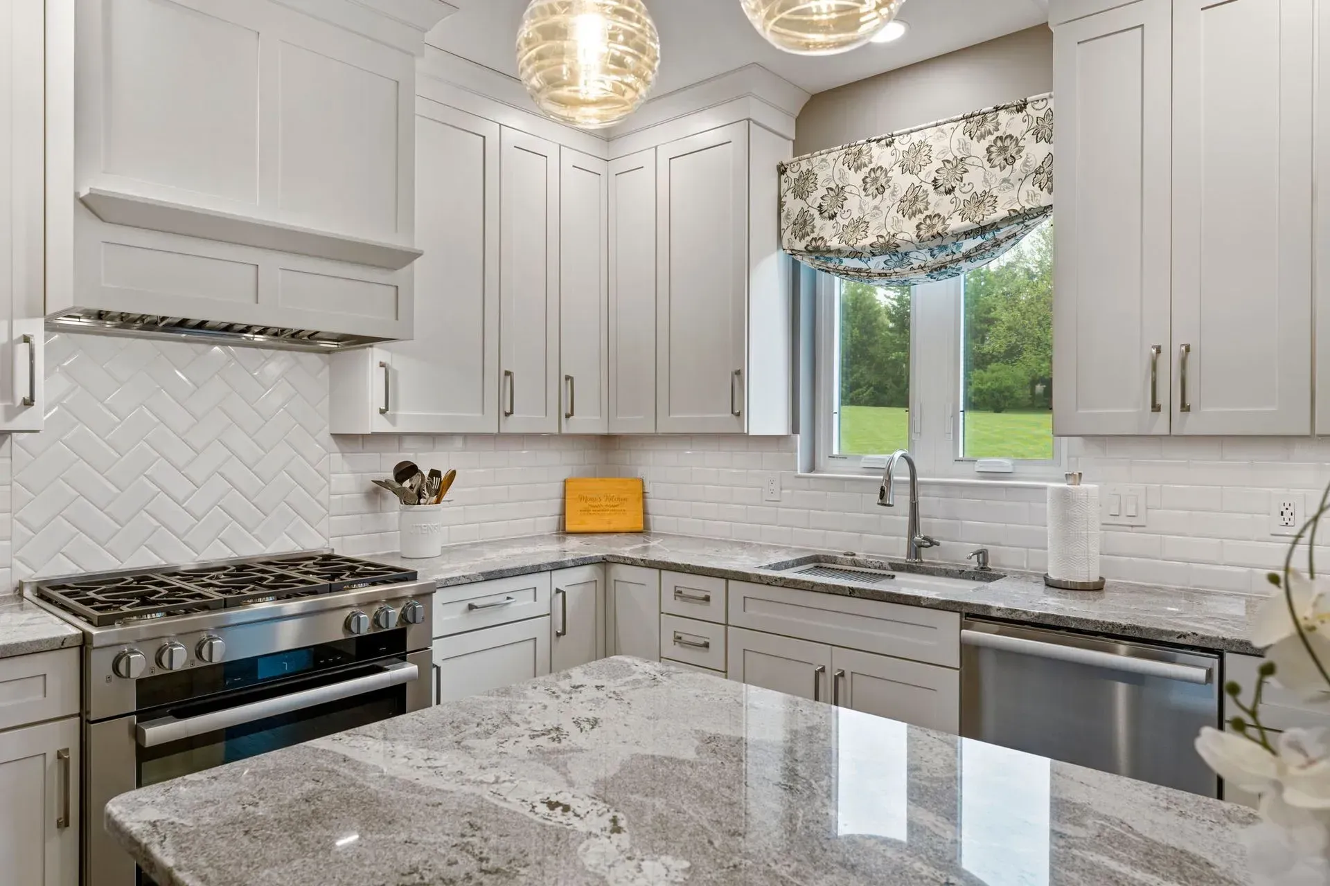 Bright modern kitchen with white cabinets, marble island, stainless appliances, and a window over the sink In Bucks Country PA