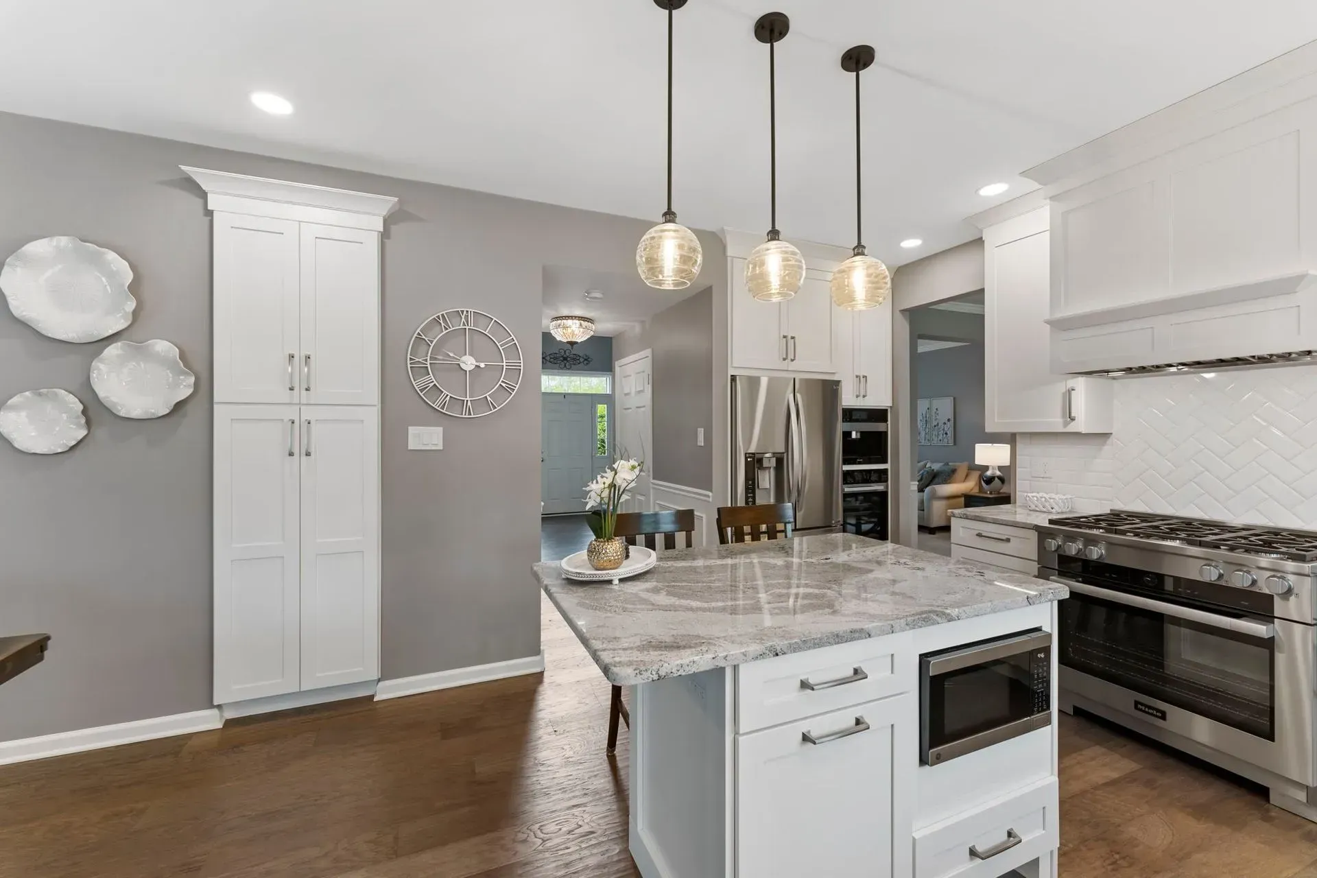 Modern white kitchen with marble island, pendant lights, stainless steel appliances, and gray walls In Bucks Country PA