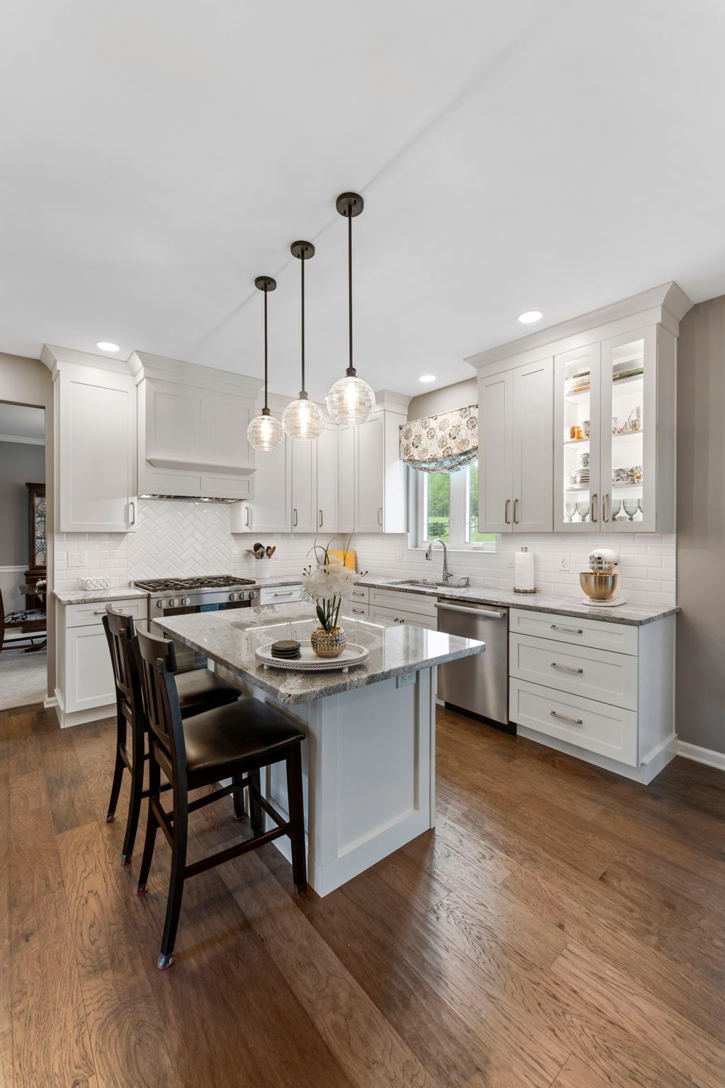 Modern white kitchen with island, pendant lights, bar stools, and hardwood floors In Bucks County PA