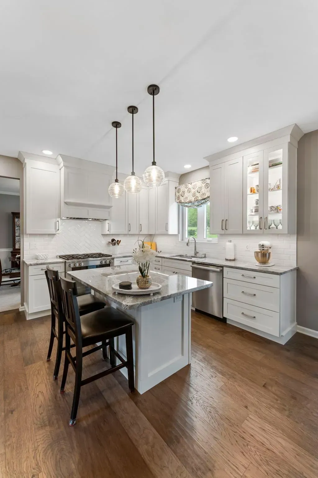Bright white kitchen with island, black stools, pendant lights, and hardwood floors In Bucks Country PA