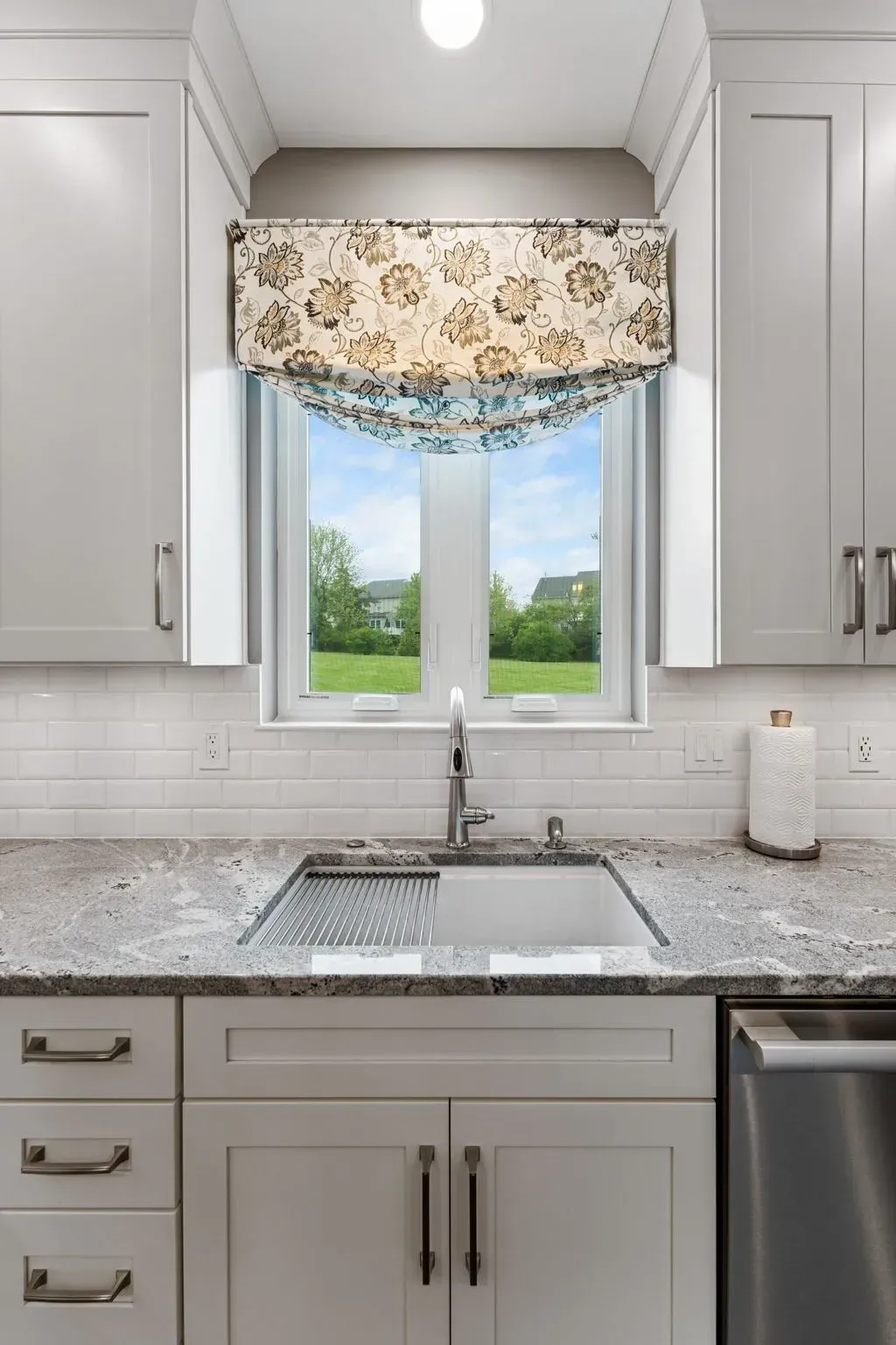 Bright kitchen sink under a window with floral valance, gray cabinets, and granite countertops In Bucks Country PA
