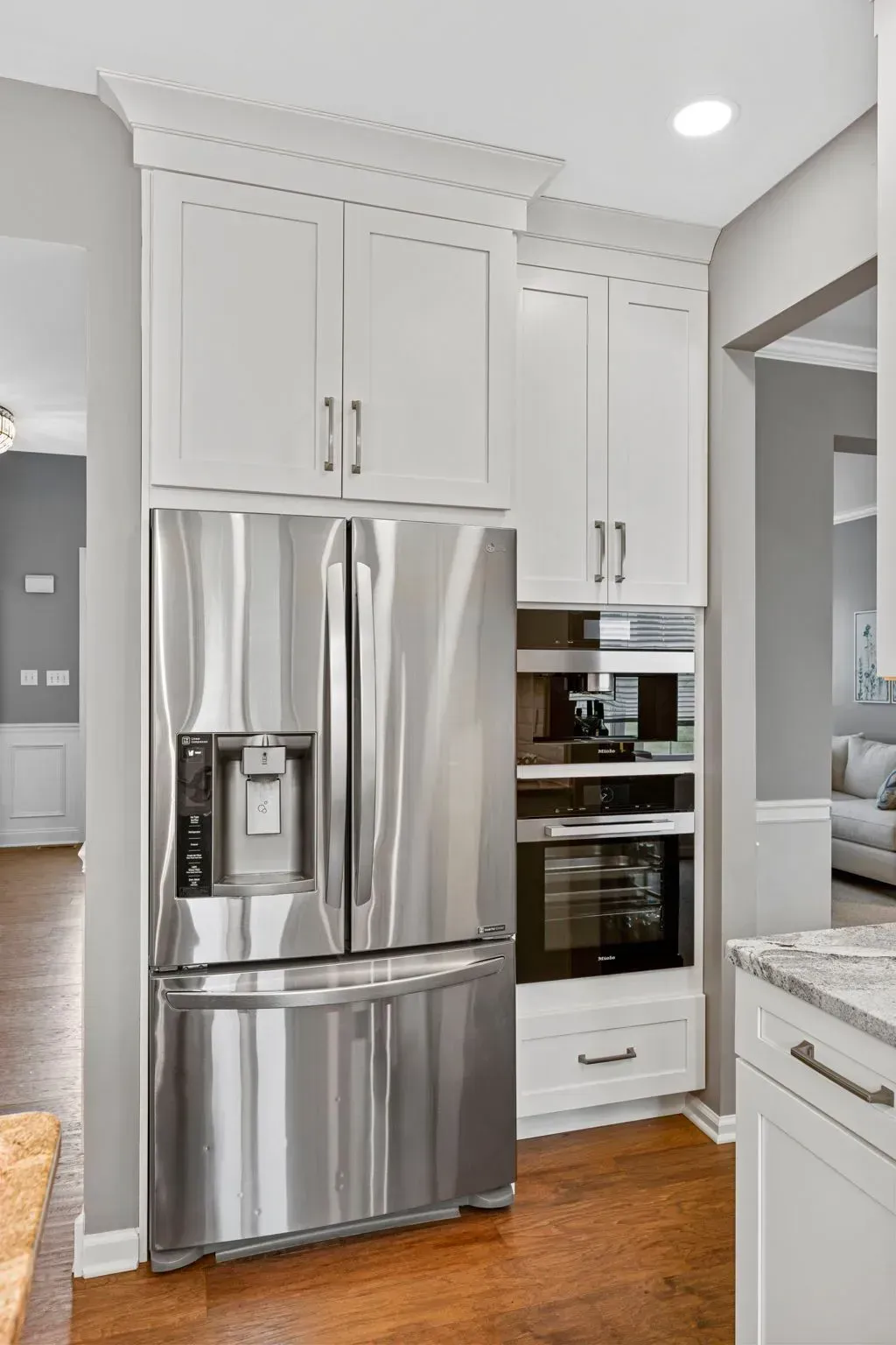 Modern white kitchen with stainless steel refrigerator, oven, and warm wood floor In Bucks Country PA