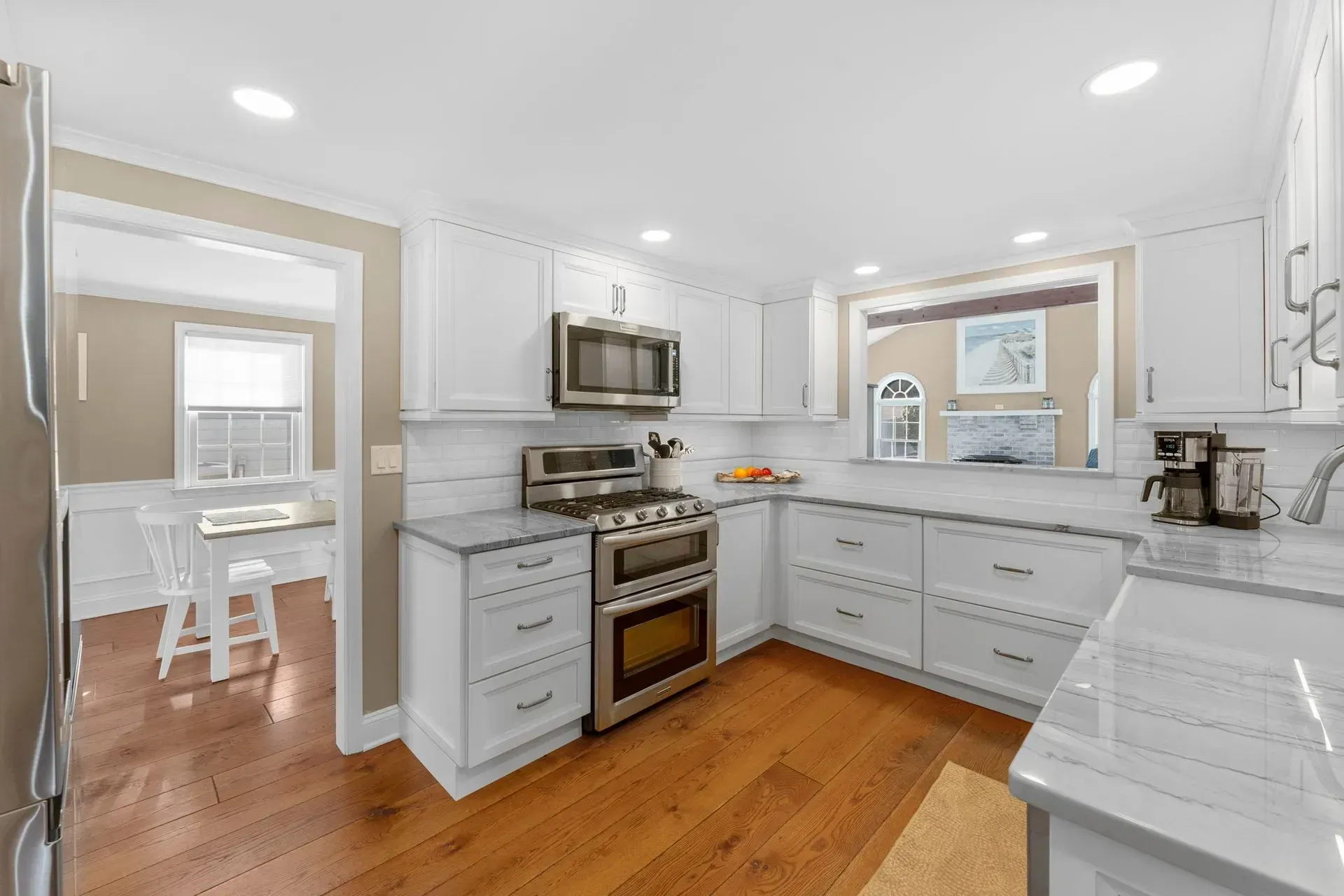 Bright white kitchen with stainless appliances, gray cabinets, wood floors, and adjoining dining area  In Bucks County PA